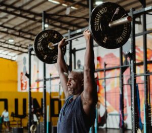 Man in Blue Tank Top Lifting a Heavy Barbell | Best Deltoid Exercises