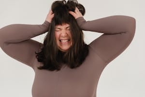 Young obese woman rumpling hair with closed eyes in white studio | placeholder for mindless eating
