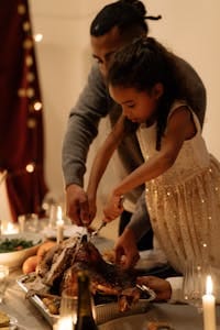 A father and daughter sharing a festive moment carving a turkey together at a holiday meal.