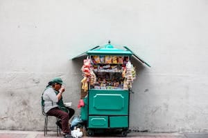 A woman enjoying a meal while sitting next to her snack cart on a city street. | This Popular Snack Could Raise Your Cancer Risk by 50%—Here’s What You Need to Know