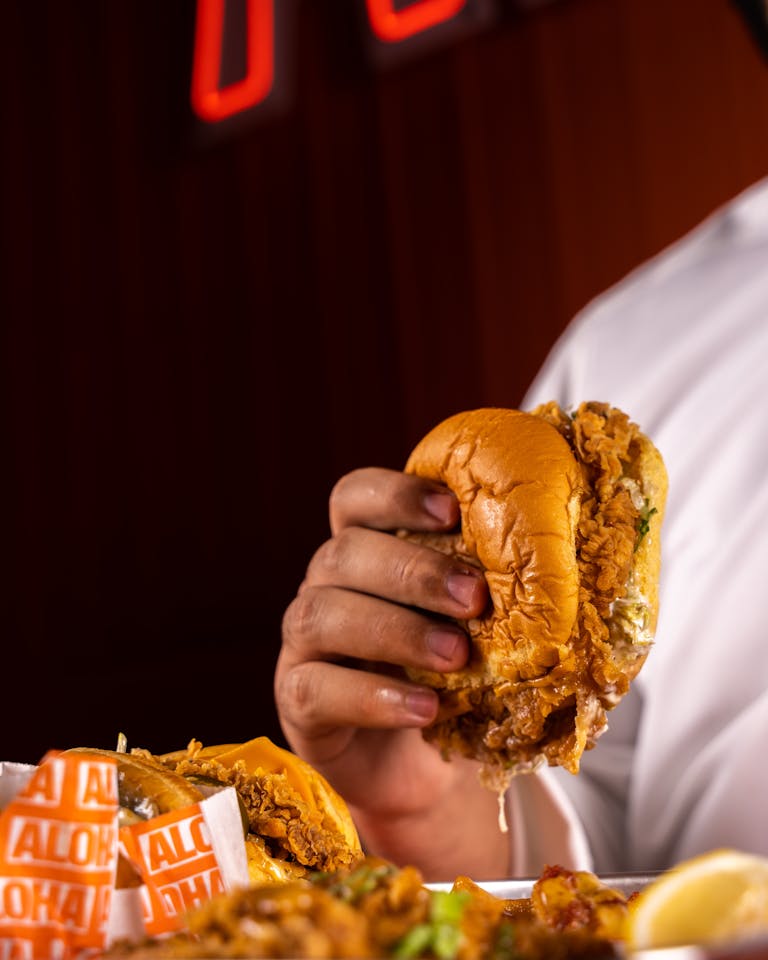 Close-up of person holding crispy fried chicken burger with a rich, savory texture. | 7 Skin-Damaging Processed Foods To Stop Eating Because They Practically Guarantee Wrinkles, According To Experts