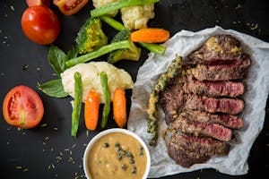 Grilled steak served with fresh vegetables and pepper sauce, presenting a colorful and appetizing meal. | 10 Must-Eat Protein Foods That Torch Fat and Sculpt Lean Muscle, According to Experts | How Much Protein You Need to Lose Weight