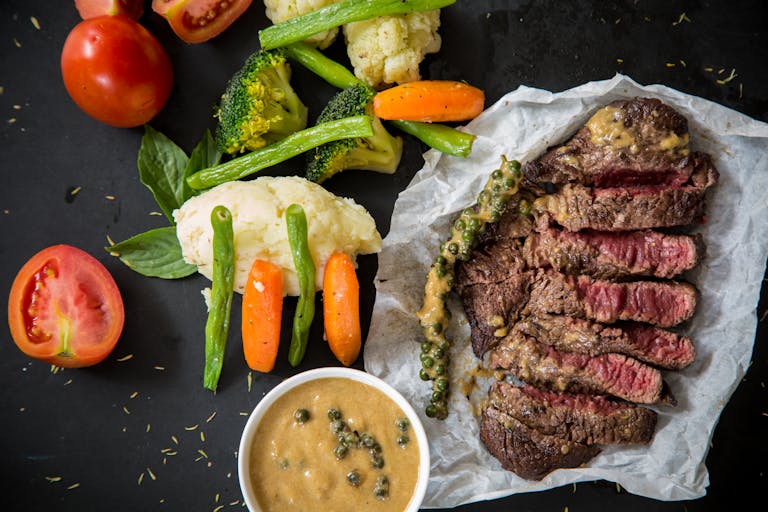 Grilled steak served with fresh vegetables and pepper sauce, presenting a colorful and appetizing meal. | 10 Must-Eat Protein Foods That Torch Fat and Sculpt Lean Muscle, According to Experts | How Much Protein You Need to Lose Weight