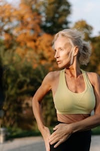 Elderly woman in sports bra practicing yoga outdoors with autumn foliage in background. | Why Working Out at This Odd Hour Could Torch Twice the Fat