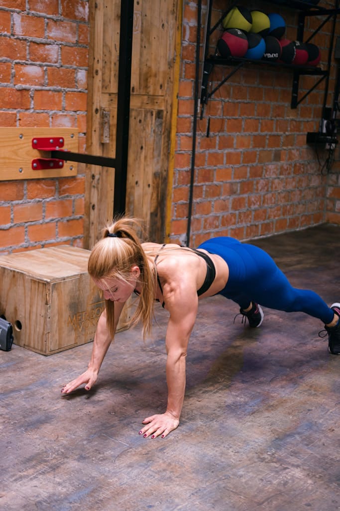 Fit woman doing push-ups in a gym with brick walls, showcasing strength and determination.