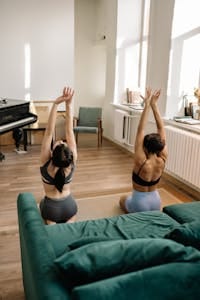 Two women in sportswear performing yoga in a cozy living room. | Too Tired for the Gym? Try This Lazy-Day Full Body Workout Hack