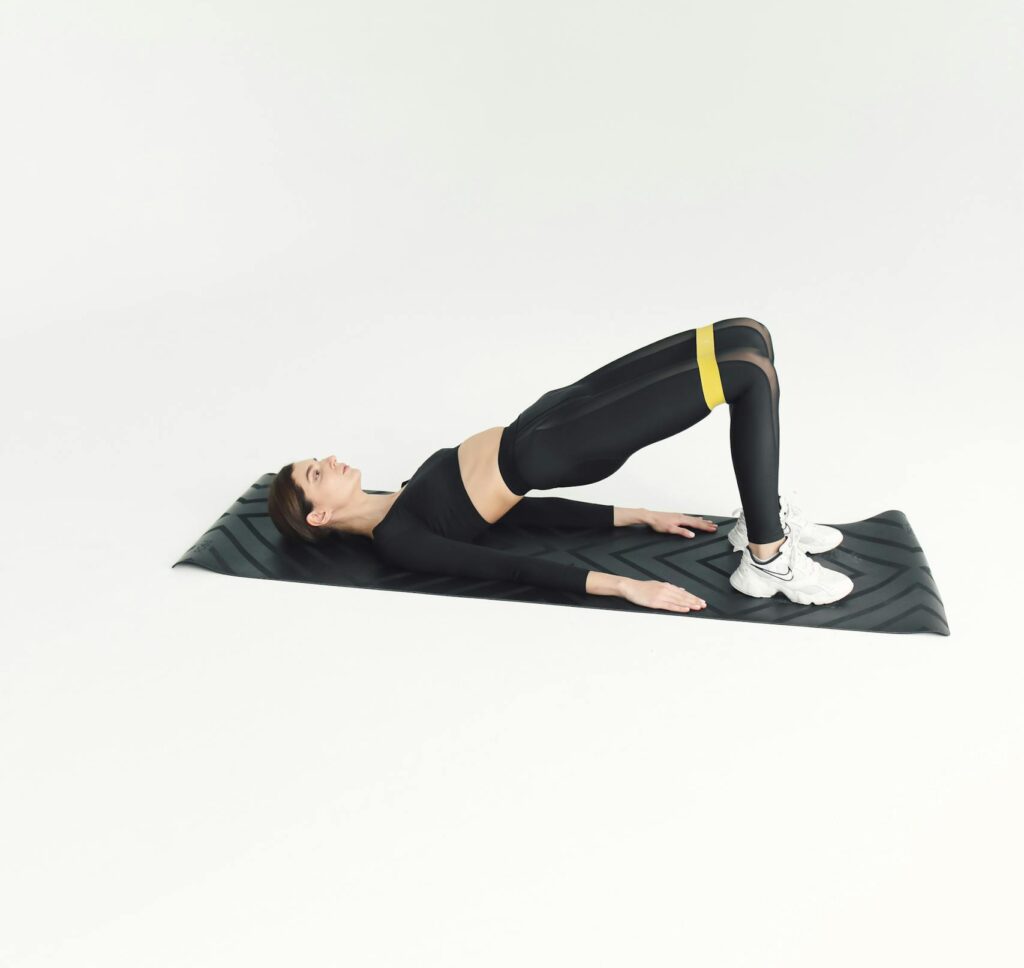 Woman doing fitness workout on mat with resistance band in studio setting. | glute bridge