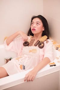 Woman relaxing in a bathtub surrounded by chocolates and candies. | Sugar Overload? Dietitians Reveal What You Should Do ASAP
