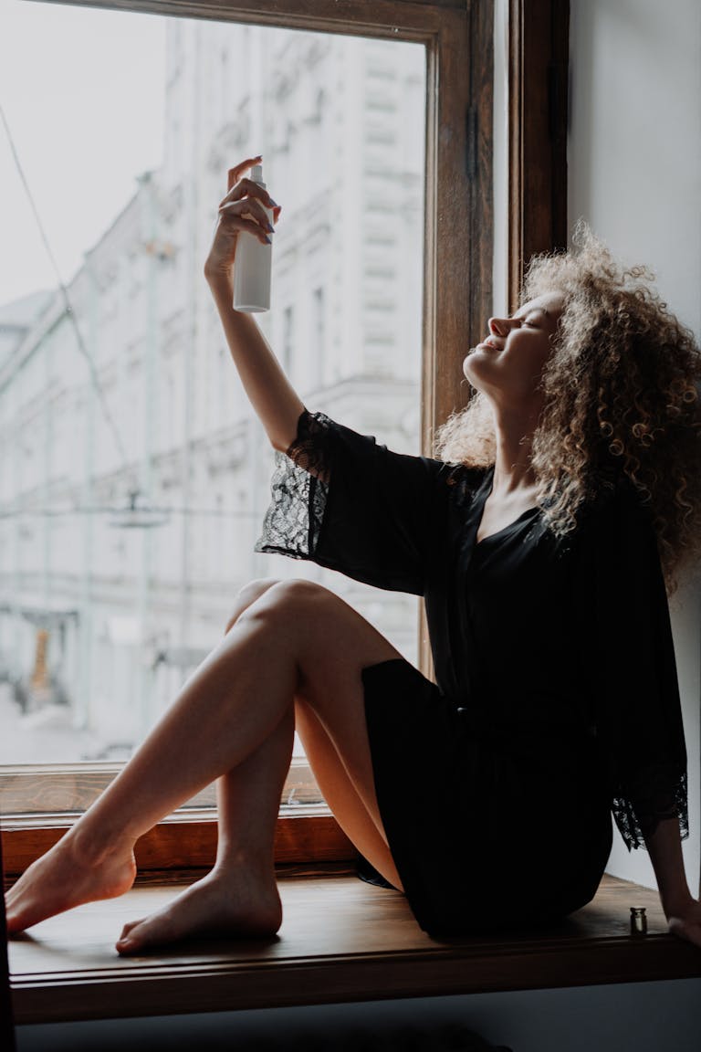 Young woman with curly hair sprays hydrating mist. Indoor beauty routine captured in natural light. | magnesium spray benefits