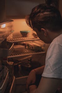 A man looks into a refrigerator, illuminated by its light during nighttime. | Can You Lose 10 Pounds in a Week? Let’s Separate Fact from Fantasy