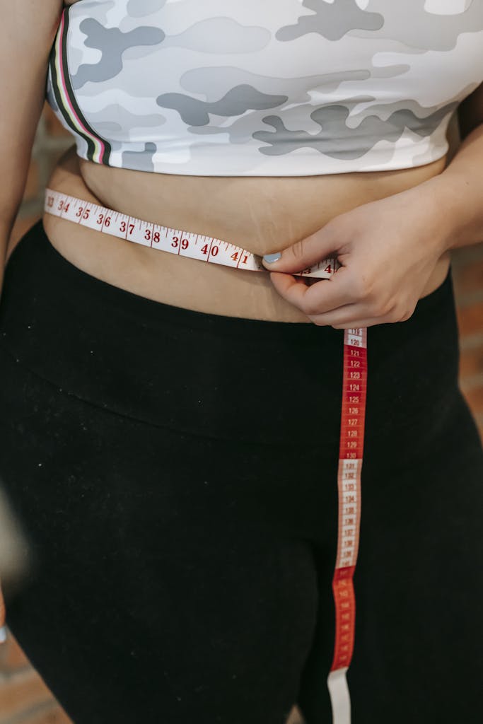 A woman measures her waist using a red measuring tape while wearing activewear. | Can You Lose 10 Pounds in a Week? Let’s Separate Fact from Fantasy
