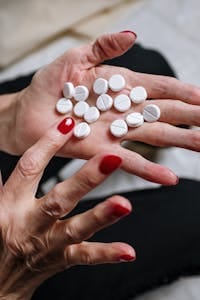 A woman's hand with red nail polish holding white pills, indicating a medical or health theme. | 5 Supplements That Won’t Help You Live Longer
