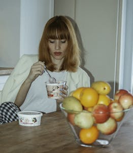 A young woman enjoys yogurt next to a bowl of fresh fruits indoors, blending health and leisure. | More Than Gut Health: The Secret Powers of Yogurt You Didn’t Know About | Cravings OUT! 10 Protein Snacks That INSTANTLY Crush Hunger & Stop Weight Gain