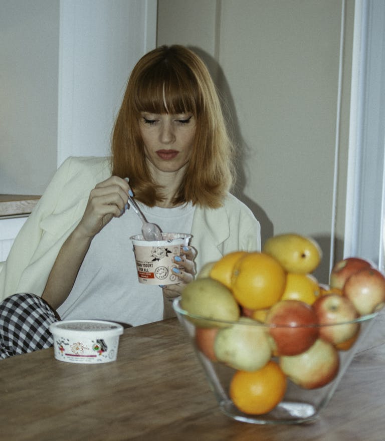A young woman enjoys yogurt next to a bowl of fresh fruits indoors, blending health and leisure. | More Than Gut Health: The Secret Powers of Yogurt You Didn’t Know About