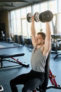 An athletic man lifting dumbbells in a well-equipped gym, showcasing fitness and strength. | Think You Need Heavy Weights for a Bigger Chest? Think Again—Here’s How to Do It with Light Dumbbells