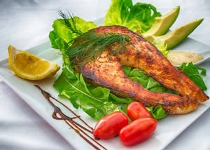 Delicious grilled salmon served with fresh vegetables and herbs on a white plate. | omega-3 foods