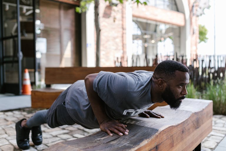 Fit bearded man doing outdoor incline push-ups on a wooden bench promoting healthy lifestyle. | Want Upper Pecs That Pop? These 3 Bodyweight Workouts Are Game-Changers