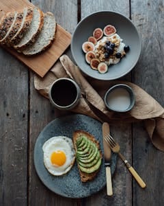 Healthy breakfast with avocado toast, eggs, and yogurt with figs and berries on a wooden table. | high protein breakfast | Ozempic-Level Weight Loss: 8 FREE Diet Hacks That CRUSH Cravings & Keep You Full (Doctor-Approved!)