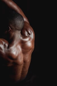 Portrait of a shirtless man flexing his muscular back in low light indoors. | Rounded Shoulders? Fix That Forever With These Game-Changing Moves