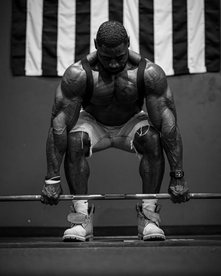 Powerful black and white image of a muscular man deadlifting a barbell in front of a flag. | Want Real Results? Just Add These 2 Exercises to Your Strength Training—Expert Approved