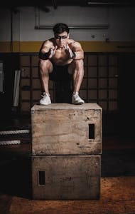 Shirtless man performing box squat in gym showcasing strength and endurance. | Want Size and Grit? This High-Intensity AMRAP Plan Is Your New Best Friend