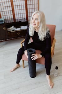 Smiling senior woman in sportswear seated indoors holding a yoga mat. | Scientists Found 10 Ways to Reverse Aging After 50—Why Aren’t We All Doing This?