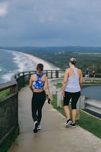 Two women walking on a coastal path with ocean views at Byron Bay, Australia, enjoying fitness and nature. | How Walking at This Specific Hour Could Help You Shed Stubborn Fat Faster