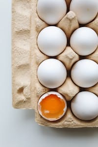 A carton of white eggs with one cracked, revealing vibrant egg yolk. Ideal for food and health themes.