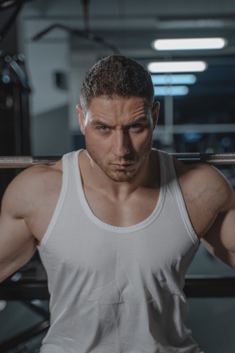 A focused man in a white tank top lifting weights in a gym setting. | Build Incredible Strength with Cluster Sets, cluster sets for strength