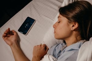 A woman sleeping peacefully in bed beside her smartphone, capturing a serene bedtime moment. | melatonin and magnesium