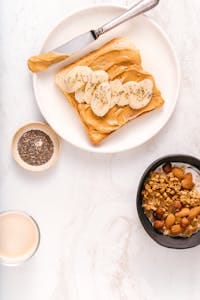 Delicious breakfast setup with peanut butter banana toast and granola bowl. | How to Get 100 Grams of Protein a Day Without Feeling Like a Gym Rat