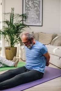 Elderly man doing yoga in living room, promoting healthy lifestyle. | These 12 Stretches Could Seriously Improve Your Sex Life—Here’s How