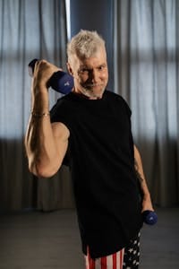 Energetic senior man working out with dumbbells indoors, promoting positive aging and wellness. | How I Changed My Workout Routine After Talking to Longevity Experts With These 5 Tips
