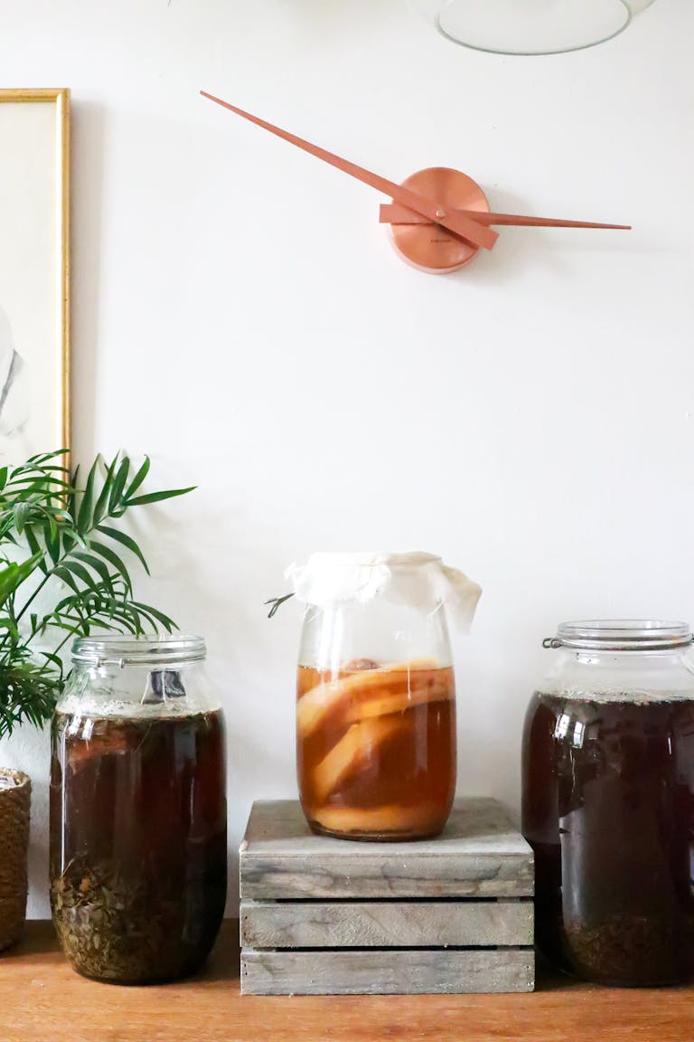 Glass jars with infused liqueurs with ingredients placed on wooden table near green plant near wall with decorations at home | Gut-Healthy Foods Recommended by RDs: Add These to Your Diet