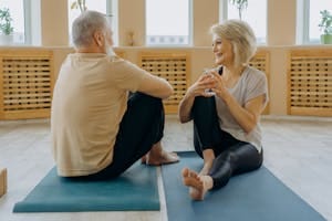 Happy senior couple sitting on yoga mats, enjoying conversation and wellness indoors. | Keep Your Body Young Forever with These Daily Stretches, Say Fitness Trainers