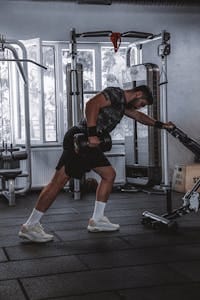 Muscular man performing dumbbell row exercise in a contemporary gym. | best dumbbell back exercises | Home Dumbbell Workouts