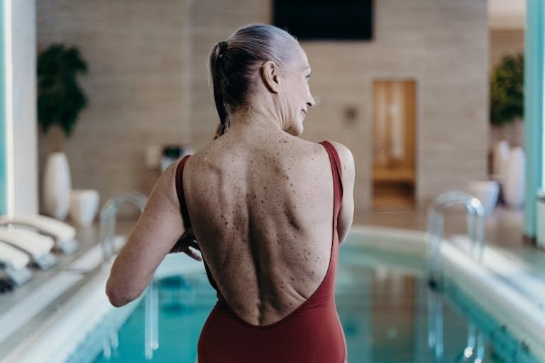 Senior woman in red swimsuit standing at indoor pool side, exuding confidence. | Transform Your Body After 50: Top Exercise Habits Revealed