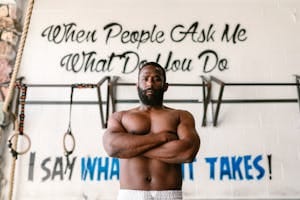 Shirtless black man standing confidently in a gym with motivational text on the wall behind him. | Unlock Rapid Muscle Growth: 5 Secret Techniques You Haven't Tried