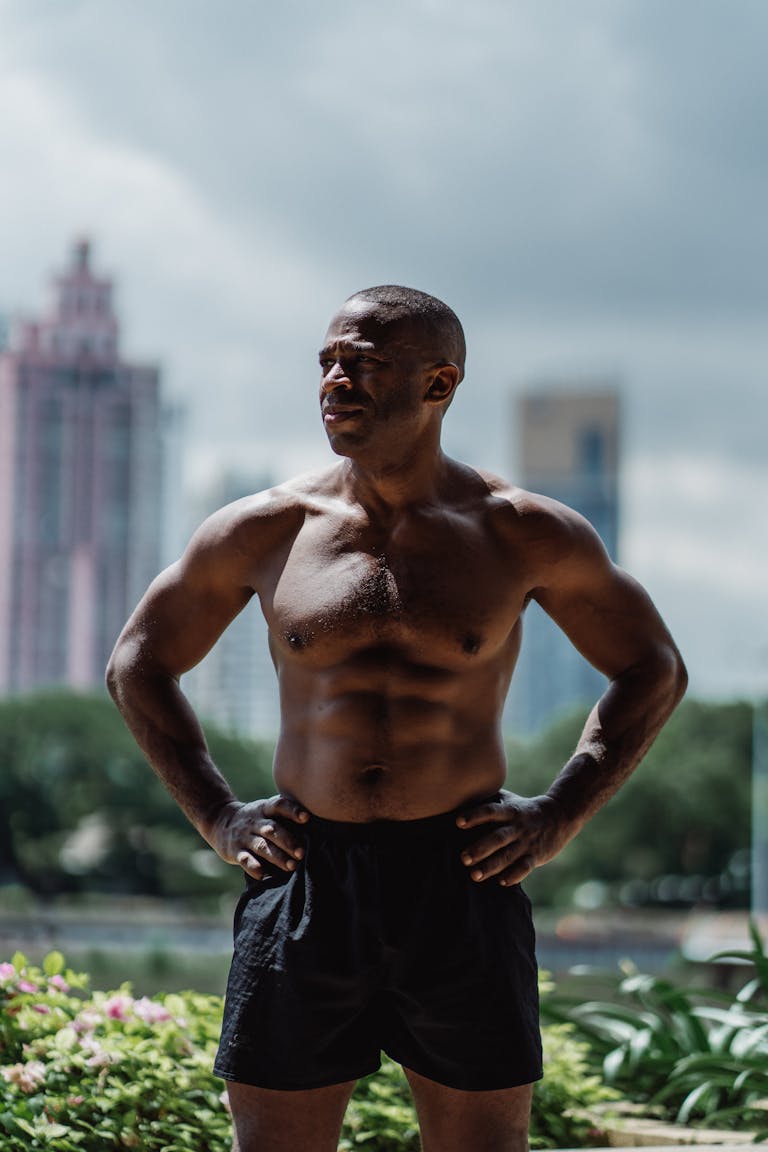 Shirtless muscular man standing confidently outdoors, showcasing fitness and strength with urban backdrop. | A Personal Trainer Reveals the Ultimate Cheat Sheet for Total-Body Fitness | 10 Super Healthy Foods You Must Eat for a Ripped Six Pack
