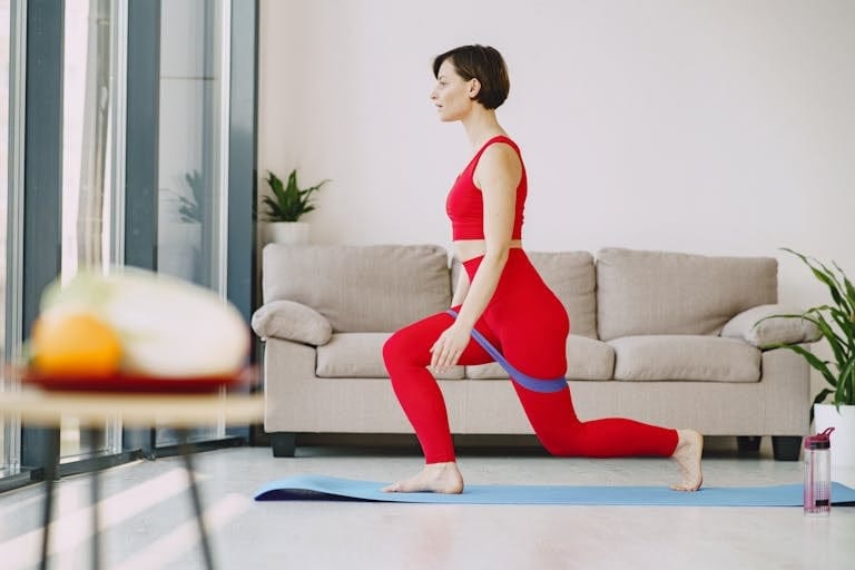 Woman in red outfit performing yoga lunge exercise indoors with resistance band. | pilates resistance bands