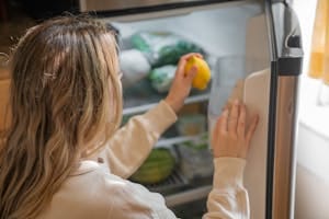 Woman reaching for a lemon in the fridge, illustrating healthy living habits. | The Key to Reducing Your Heart Disease Risk May Already Be in Your Fridge