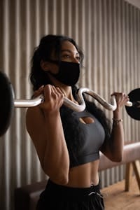 Young sporty female in activewear and face mask exercising with barbell in gym | This Is How Disgusting Your Gym Equipment Actually Is—And No One’s Talking About It