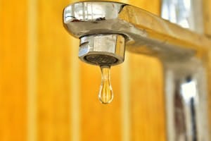 A close-up shot of a water droplet hanging from a stainless steel faucet, highlighting surface tension. | You’re Drinking Plastic! This Simple Trick Removes 99% in Minutes
