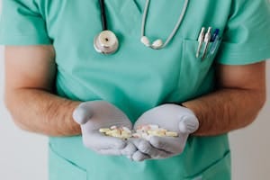 A healthcare professional in uniform holding a variety of pills in gloved hands. | Heart-Boosting Supplements a Cardiac Surgeon Swears By: CoQ10, Omega-3, and More