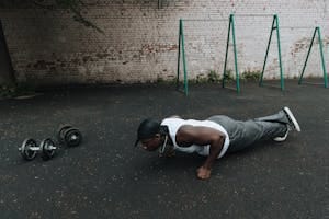 A man in sports attire doing push-ups on an outdoor asphalt surface beside dumbbells. | How to Turn Ordinary Pushups Into a Muscle-Building Power Move