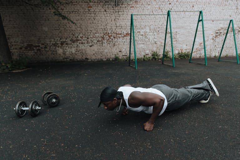 A man in sports attire doing push-ups on an outdoor asphalt surface beside dumbbells. | How to Turn Ordinary Pushups Into a Muscle-Building Power Move