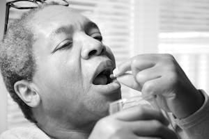 A senior man taking medicine with a glass of water indoors. Black and white photo. | The Cheap Daily Supplement That’s Boosting Brainpower in Older People