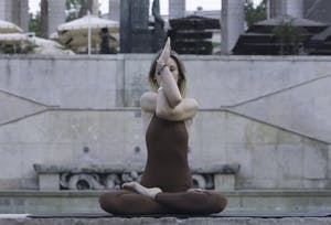 A young woman meditates in a yoga pose by an outdoor fountain, promoting relaxation. | The 3 Seated Yoga Poses You Should Be Doing Right Now for Better Flexibility