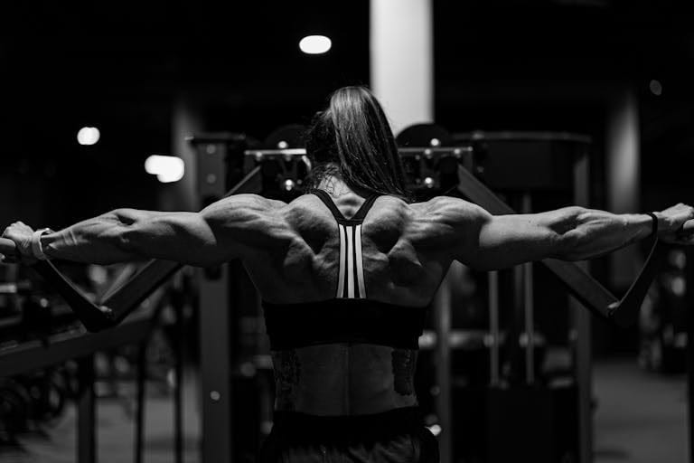 Black and white photo of a strong woman exercising in a gym with focus on back muscles. | Want Strong, Toned Arms? Try This Trainer’s 8-Exercise Routine Today | Back Day Breakthrough: Why Trainers Are Begging You to Add This Game-Changing Move