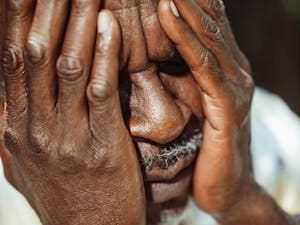 Close-up portrait of an elderly man with hands covering face, showing emotion. | Why the Risk of Dying from This Disease Increases After 50—And How to Prevent It